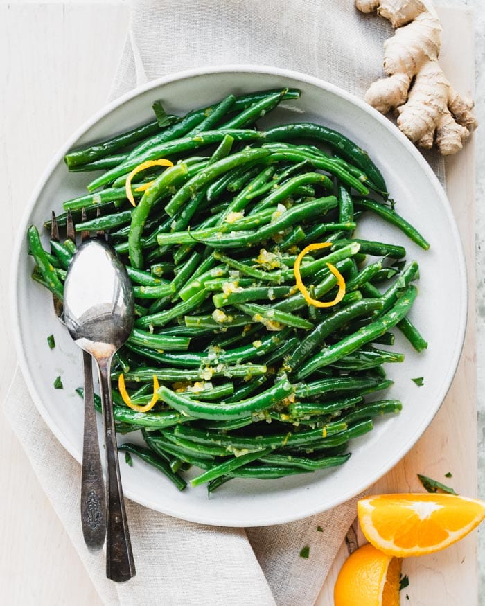 an overhead view of a round platter of green beans with orange zest