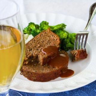 two slices of barbecued beef meatloaf with barbecue sauce on them, with mashed potatoes and broccoli
