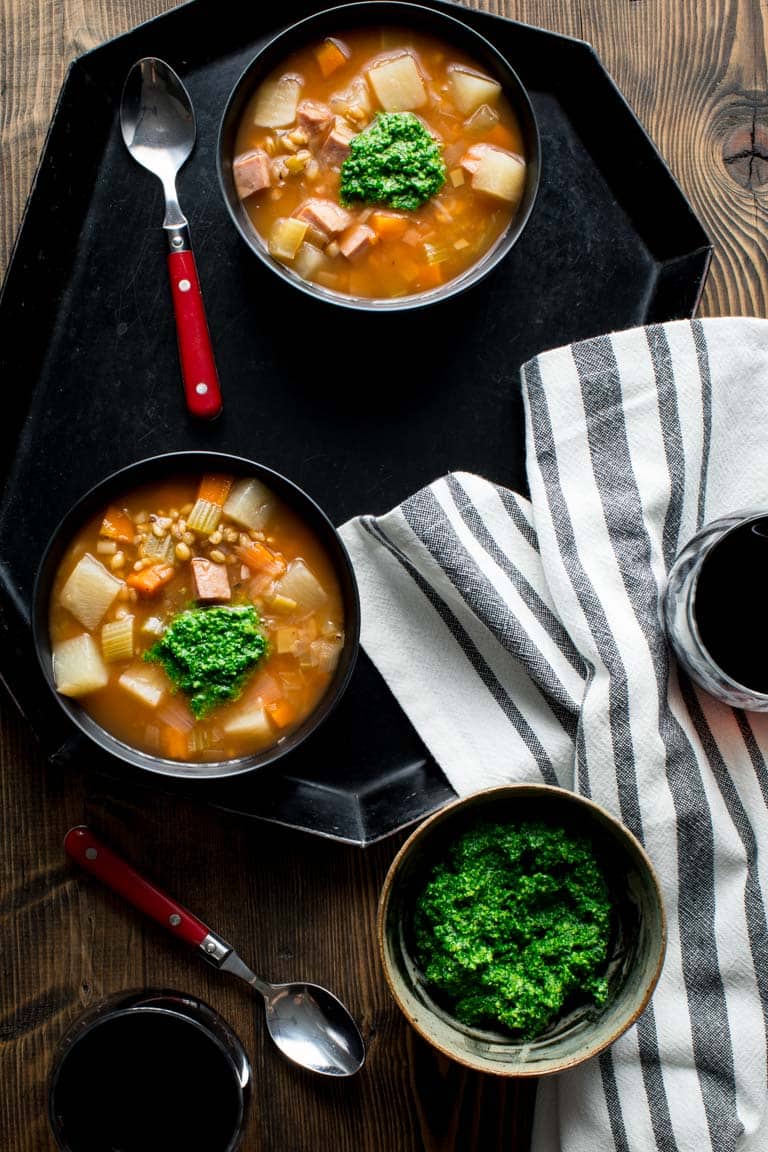 overhead shot of two soup bowls full of ham, barley, vegetables, and spinach pesto