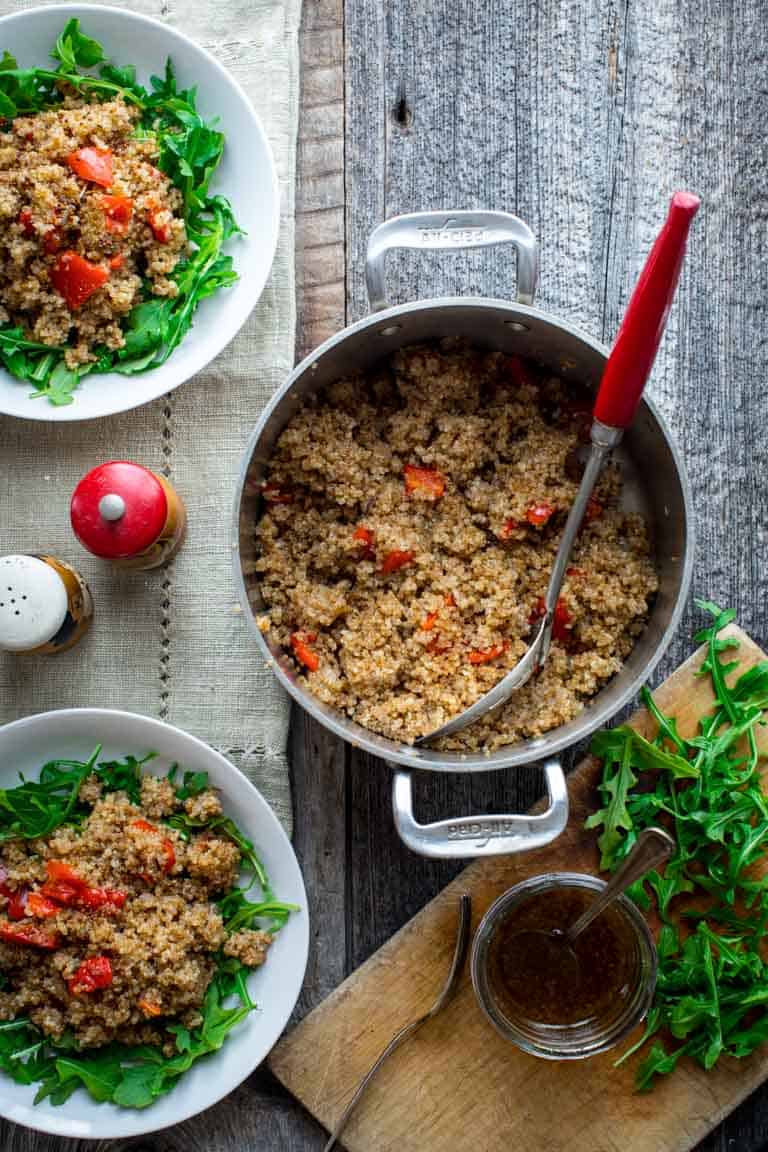 Quinoa Arugula Salad in a pot with a serving spoon and two plated bowls alongside