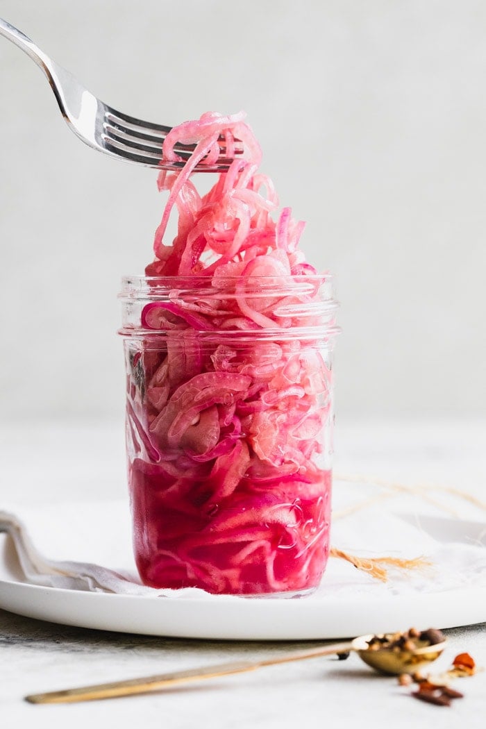 a jar of pickled red onions from the side, a fork lifting up strands of the onion