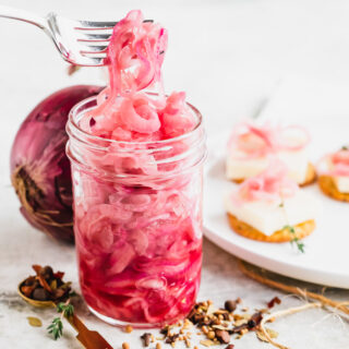 a jar of pickled red onions from the side, a fork lifting up strands of the onion