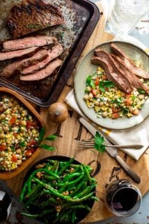 a table scape with a tray of grilled steak, green beans, a bowl of corn salad and a plate with both from overhead