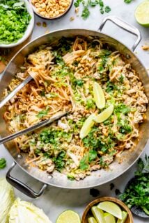 a metal saute pan with stir fried noodles and fresh herbs from overhead with tongs