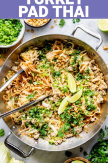 a metal saute pan with stir fried noodles and fresh herbs from overhead with tongs