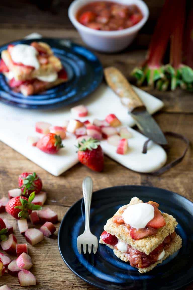 Strawberry shortcake on a plate next to a cutting board with strawberries and rhubarb