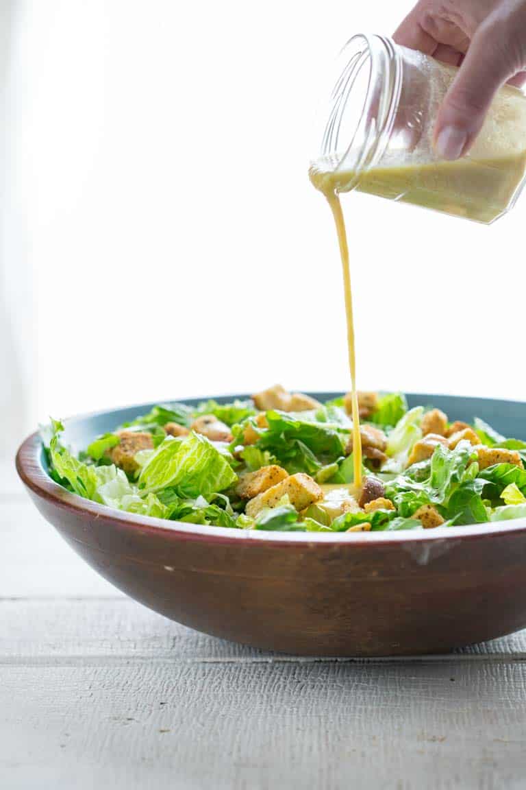 Caesar Dressing being poured over a Caesar salad