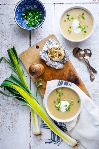two bowls of soup with leeks and scallions and a bulb of roasted garlic