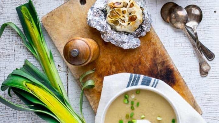 two bowls of soup with leeks and scallions and a bulb of roasted garlic