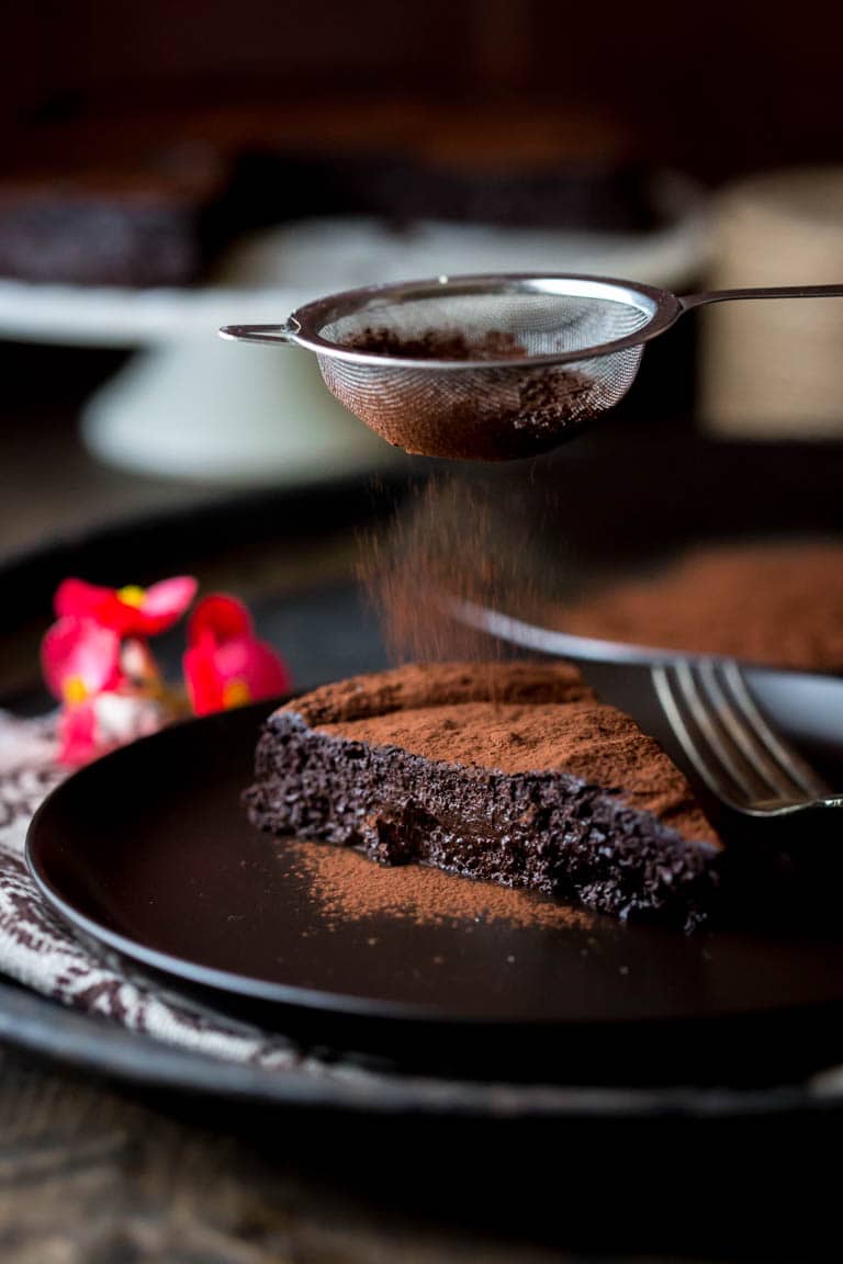 dusting cocoa powder onto a slice of Flourless Chocolate Cake