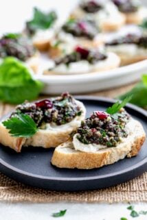 cranberry pesto crostini on a black plate with a platter of them in the background