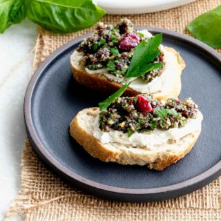 two crostini with parsley sprigs on a black appetizer plate