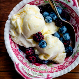 corn ice cream in a pink and white dish with fresh berries on top