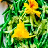 the green beans with the basil dressing drizzled over it up close with a few edible flowers on top