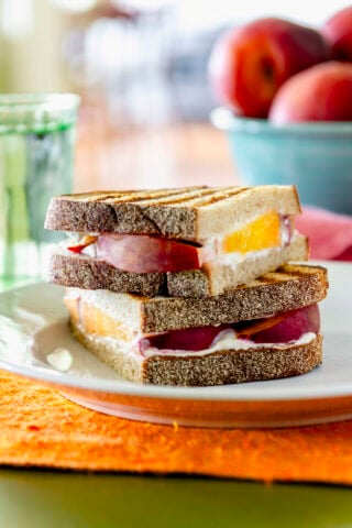 peach goat cheese panini sandwich cut in half and stacked on a plate on top of an orange placemat