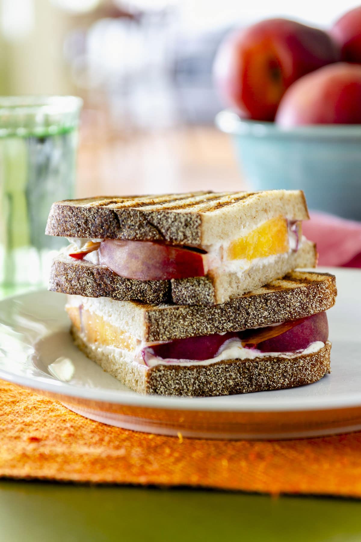 peach goat cheese panini sandwich cut in half and stacked on a plate on top of an orange placemat
