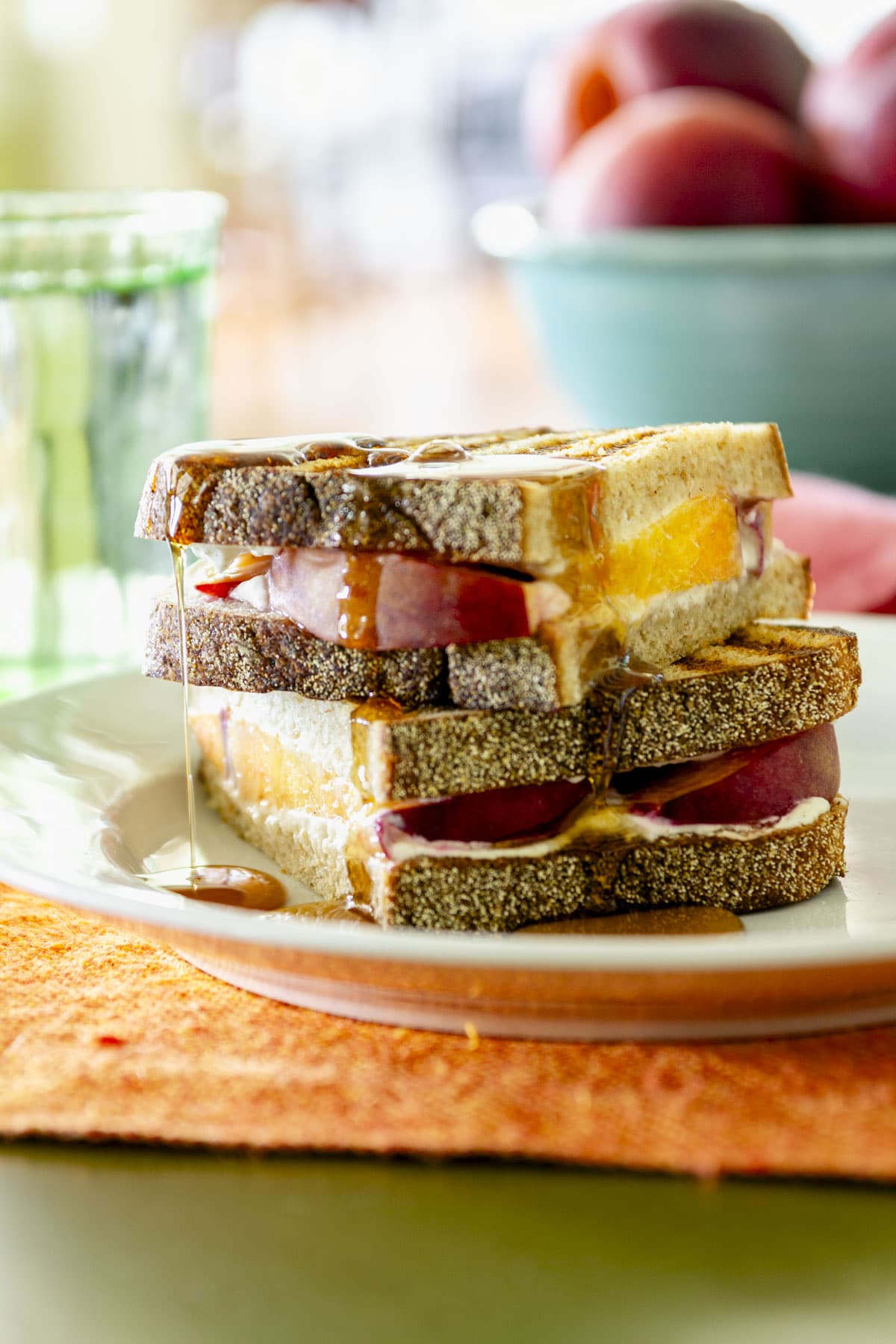 peach goat cheese panini sandwich cut in half and stacked on a plate on top of an orange placemat