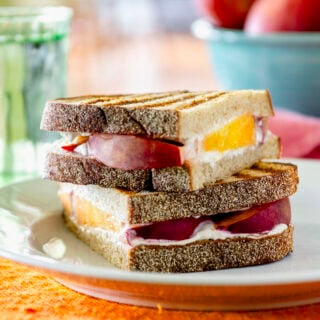 peach goat cheese panini sandwich cut in half and stacked on a plate on top of an orange placemat
