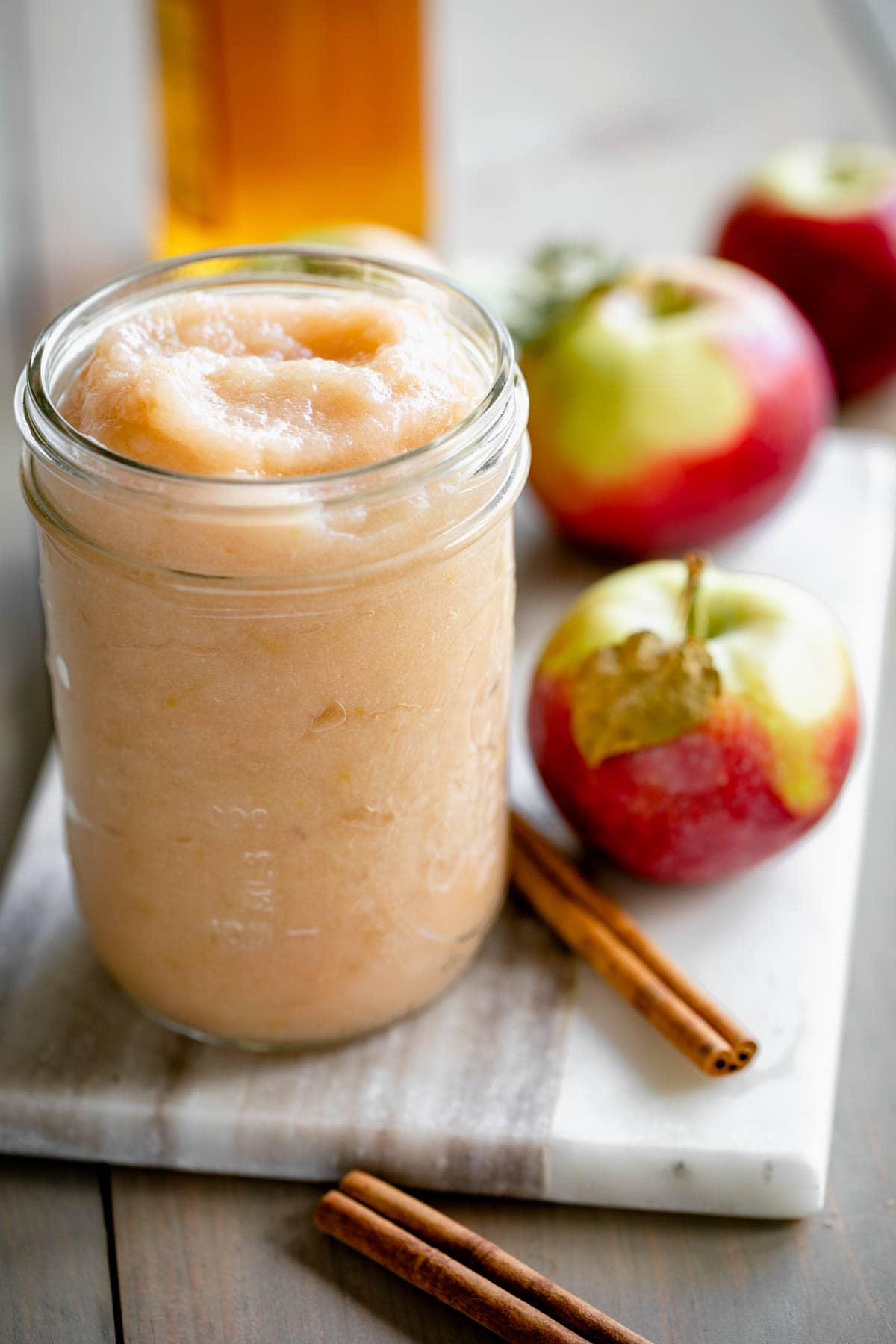 a jar of homemade applesauce on a white marble board with an apple and cinnamon stick