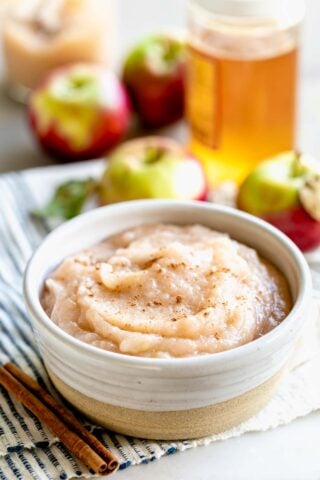 a ceramic dish of applesauce with a jar of honey and apples on a blue and white dish cloth