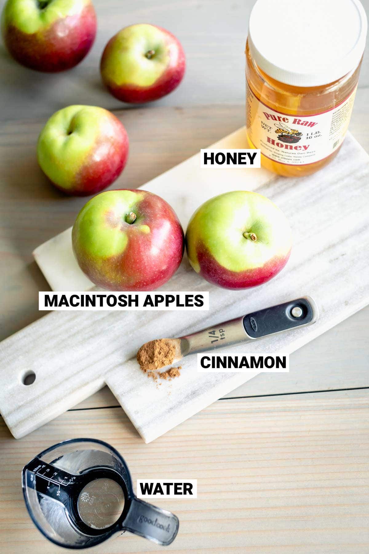 apples, jar of honey, spoonful of cinnamon and a pitcher of water on a white marble cutting board