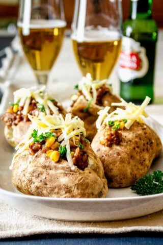 loaded baked potatoes on a platter with cheese on top and glasses of beer in the background