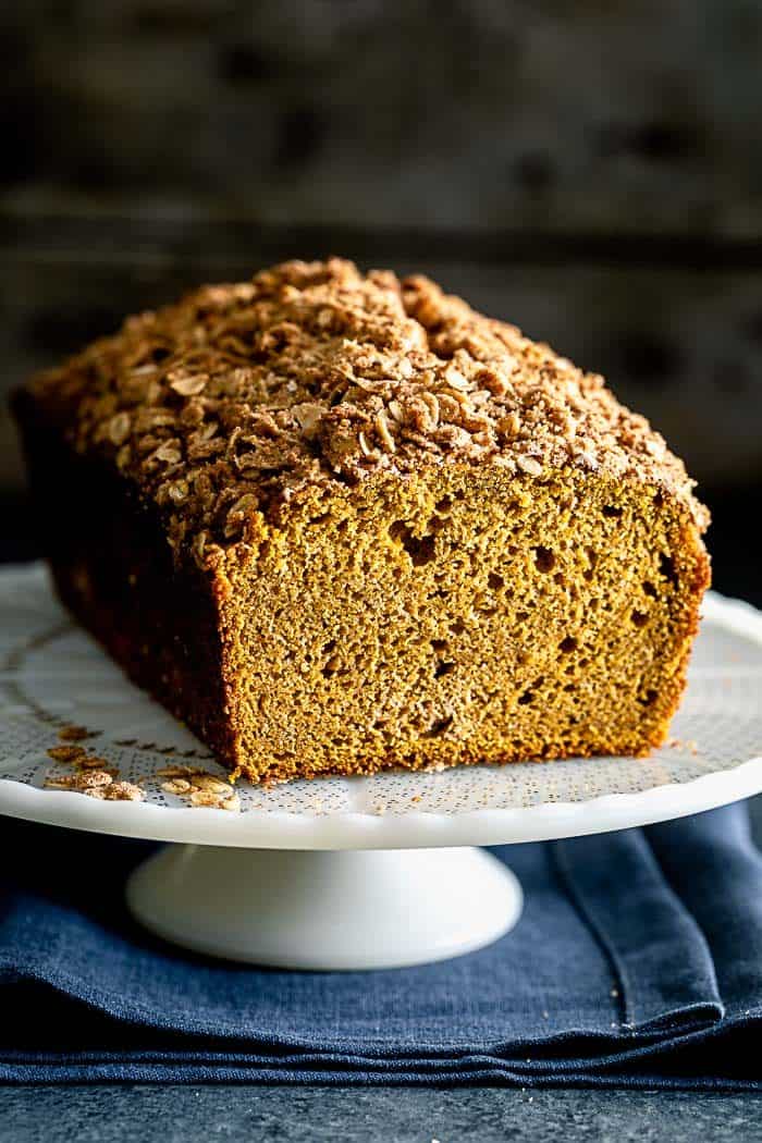 A loaf of pumpkin streusel bread on a cake stand, with a slice removed to reveal the texture of the crumb