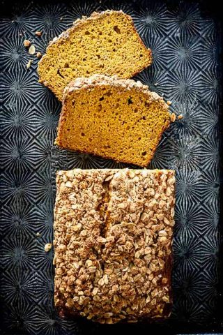 A loaf of pumpkin streusel bread, cut into slices and laid on a black patterned baking sheet
