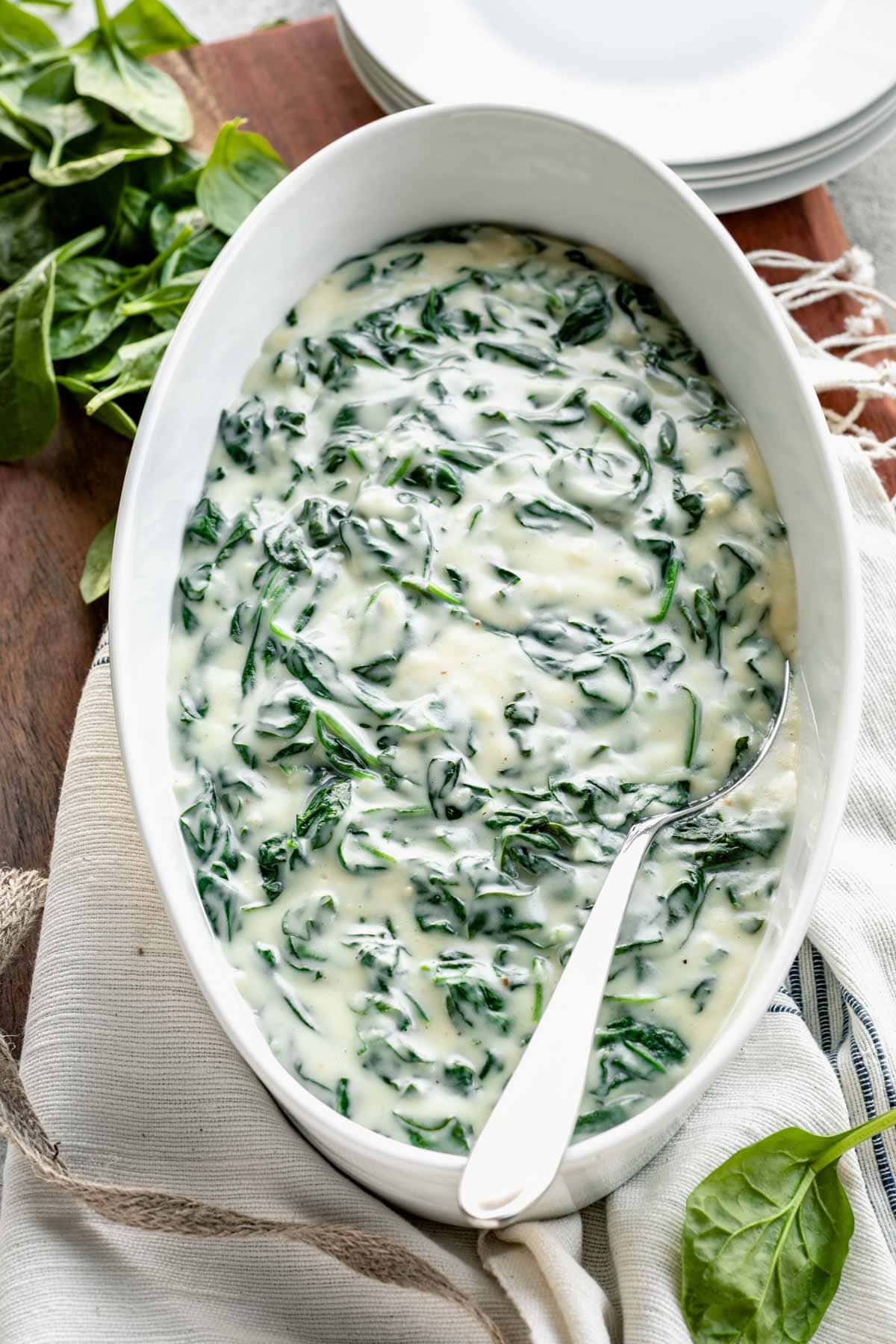 creamed spinach in oval white serving dish with silver serving spoon