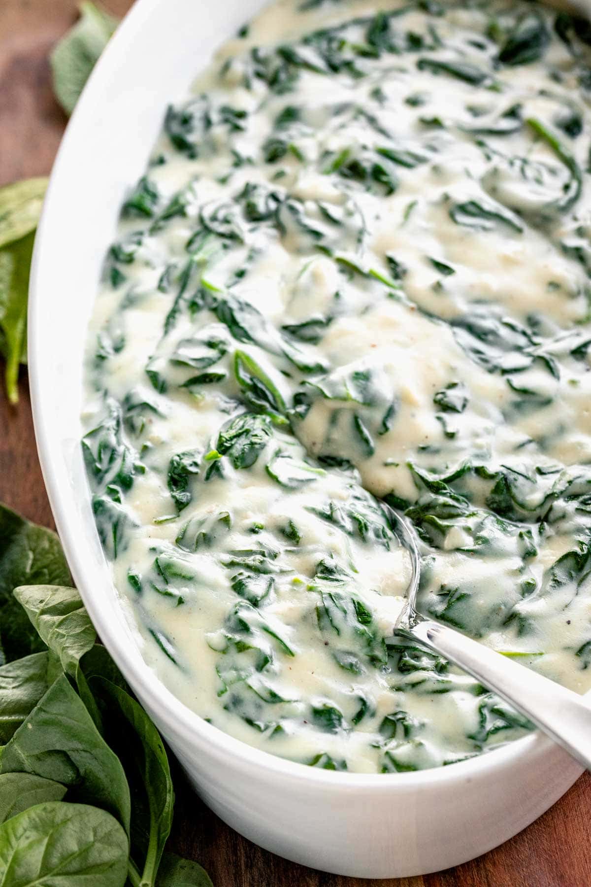 overhead shot of creamed spinach in oval white serving dish with silver serving spoon