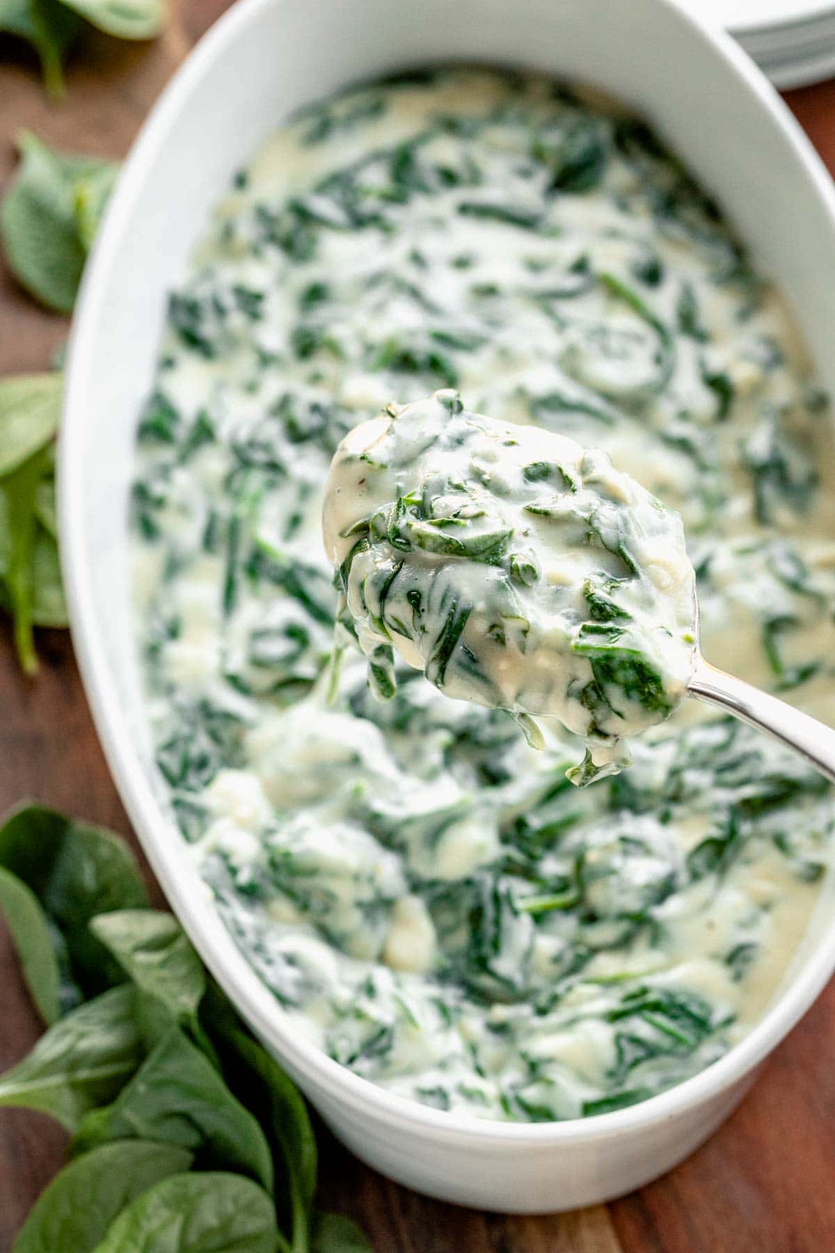 overhead shot of creamed spinach in oval white serving dish with close-up of spoonful of creamed spinach