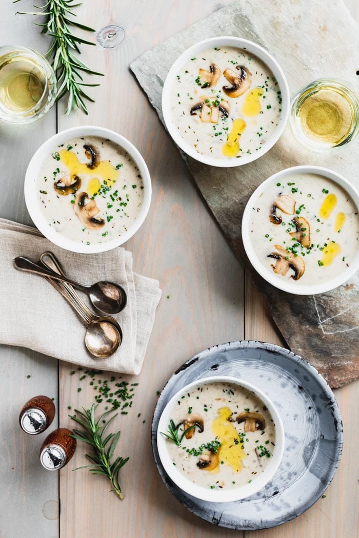 bowls of mushroom soup on a wooden table with fresh rosemary sprigs