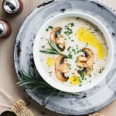Cream of mushroom soup in a white bowl set on a gray pie plate on a brownish gray wooden tabletop