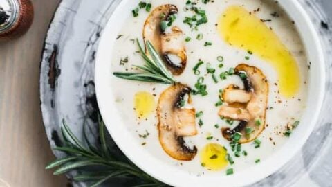 Cream of mushroom soup in a white bowl set on a gray pie plate on a brownish gray wooden tabletop