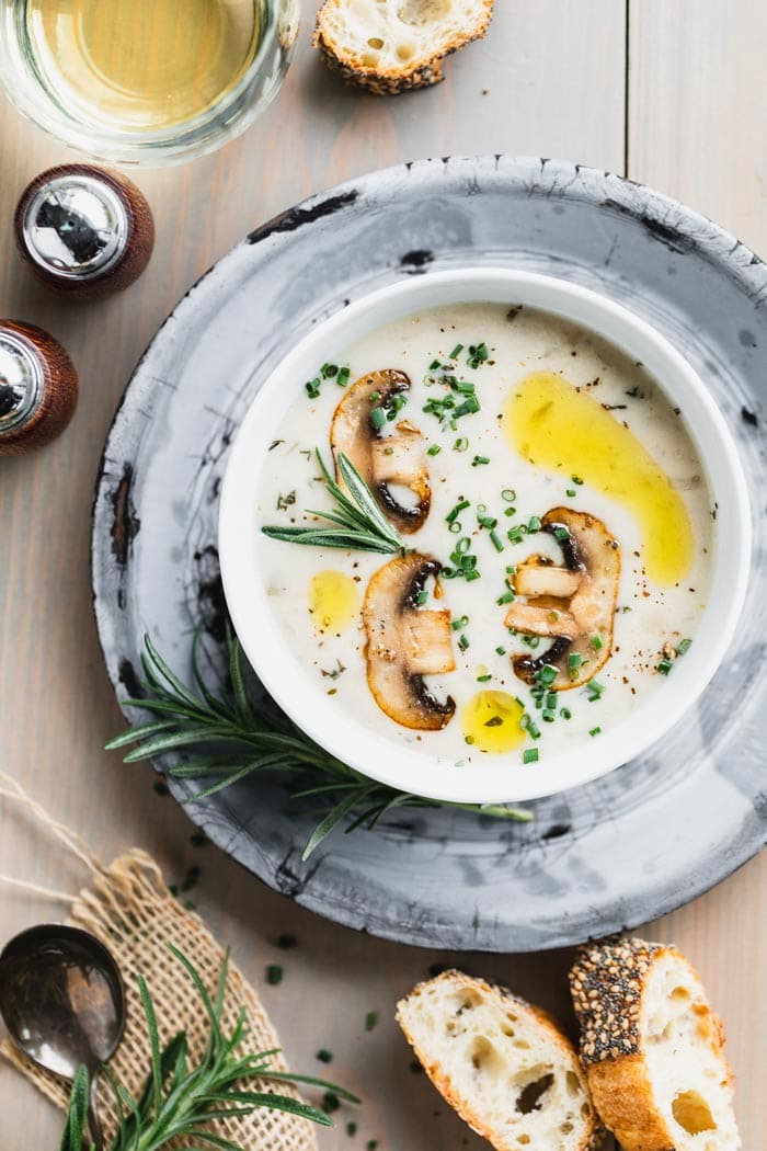 Cream of mushroom soup in a white bowl set on a gray pie plate on a brownish gray wooden tabletop