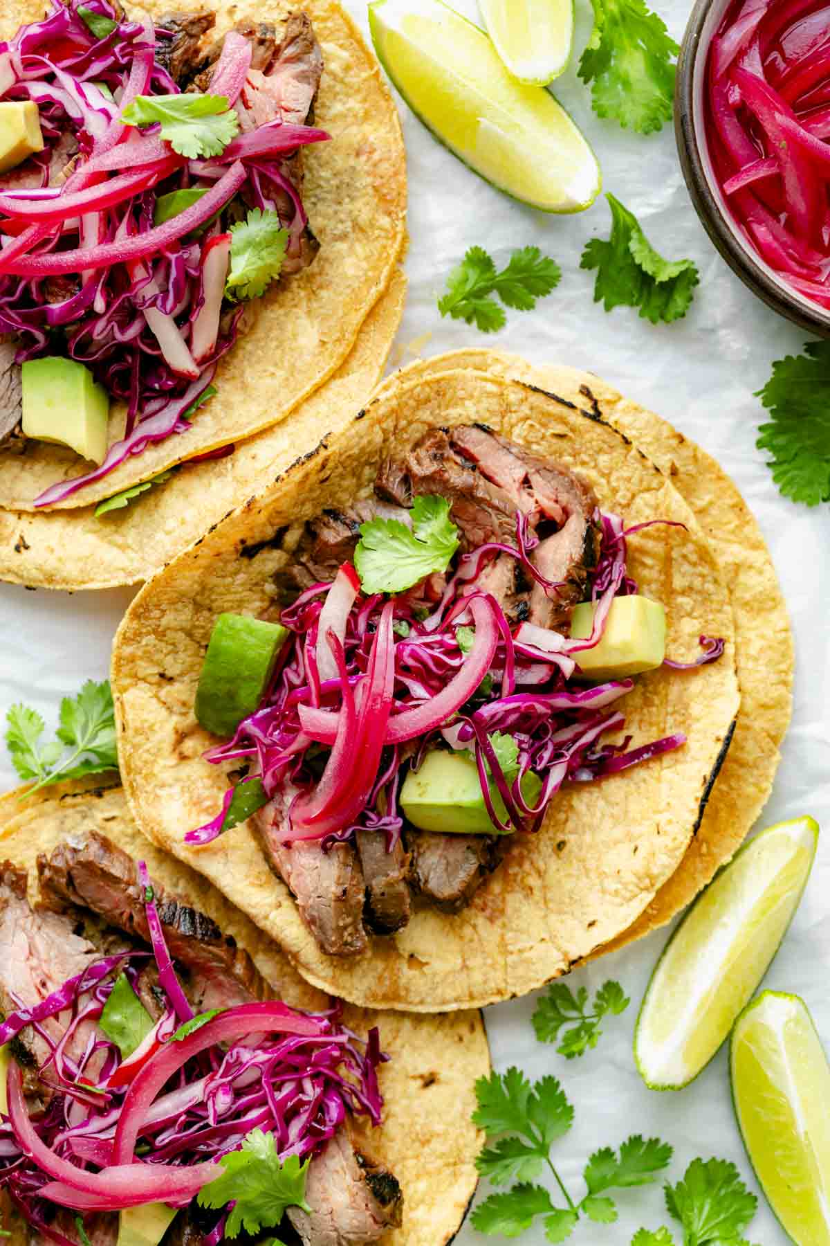 three of the steak tacos on corn tortillas with pickled onions