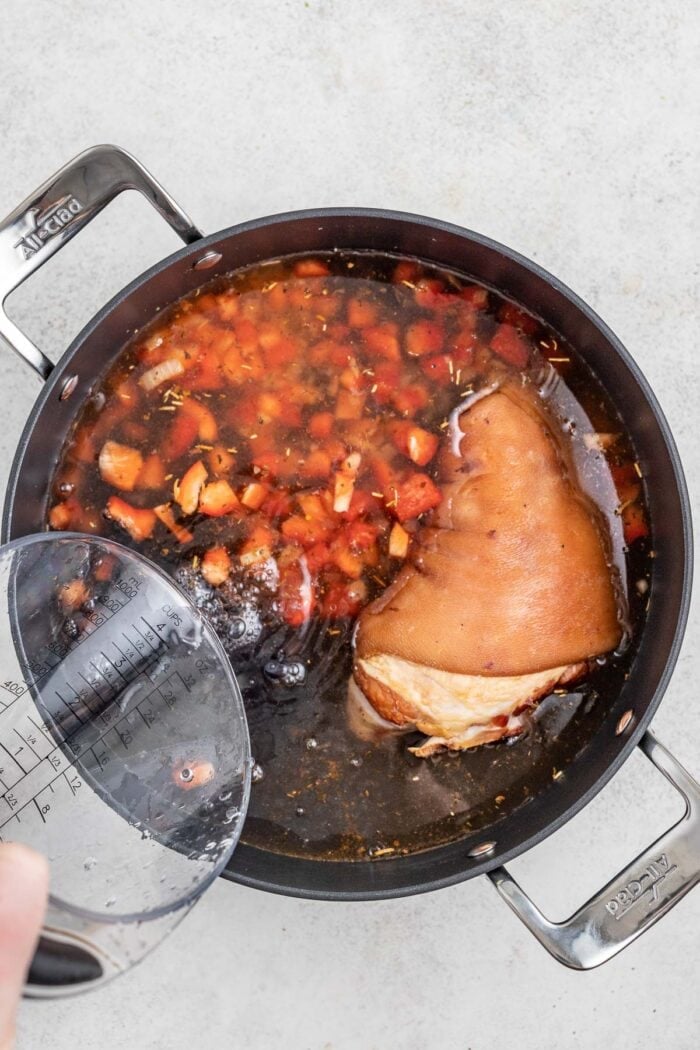 pouring water over the sauteed veggies, soaked beans and the ham hock
