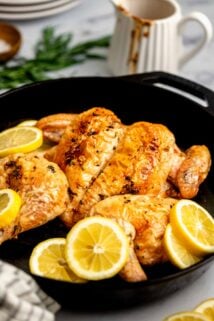 cast iron skillet with the spatchcocked chicken in it with lemon wedges
