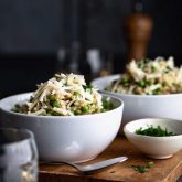 A side view of two bowls of brown rice risotto with peas and topped with white cheddar cheese