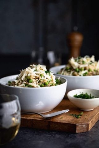 A side view of two bowls of brown rice risotto with peas and topped with white cheddar cheese