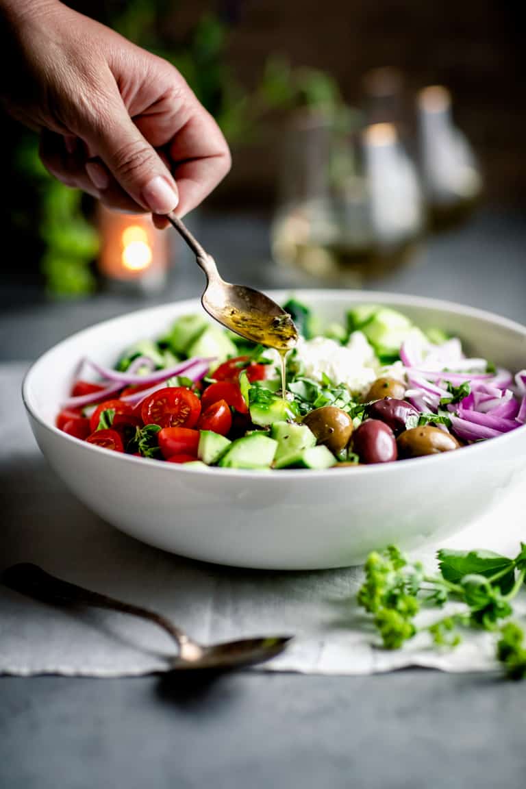 A spoonful of dressing being drizzled over the chopped Greek Cucumber Salad
