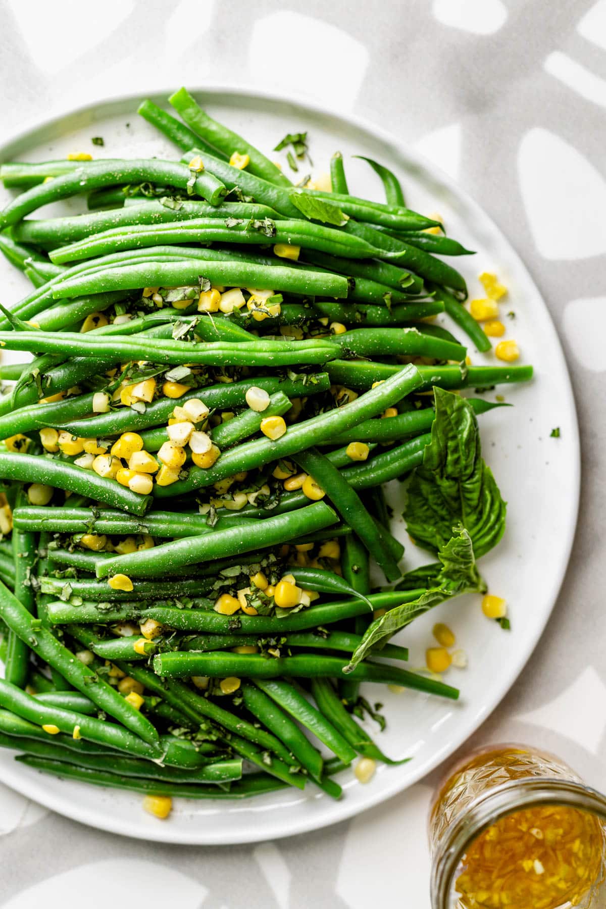 the green beans with the corn on a white round platter with a jar of the salad dressing on the side