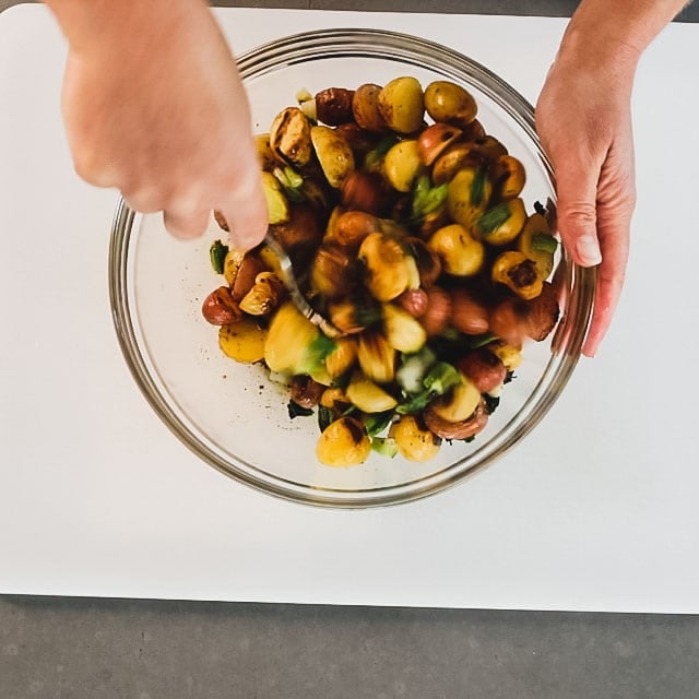 stirring potatoes and scallions with the dressing