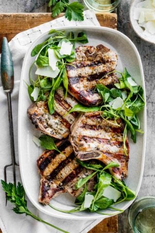 a platter of pork chops with arugula salad from overhead on a table with a large serving fork
