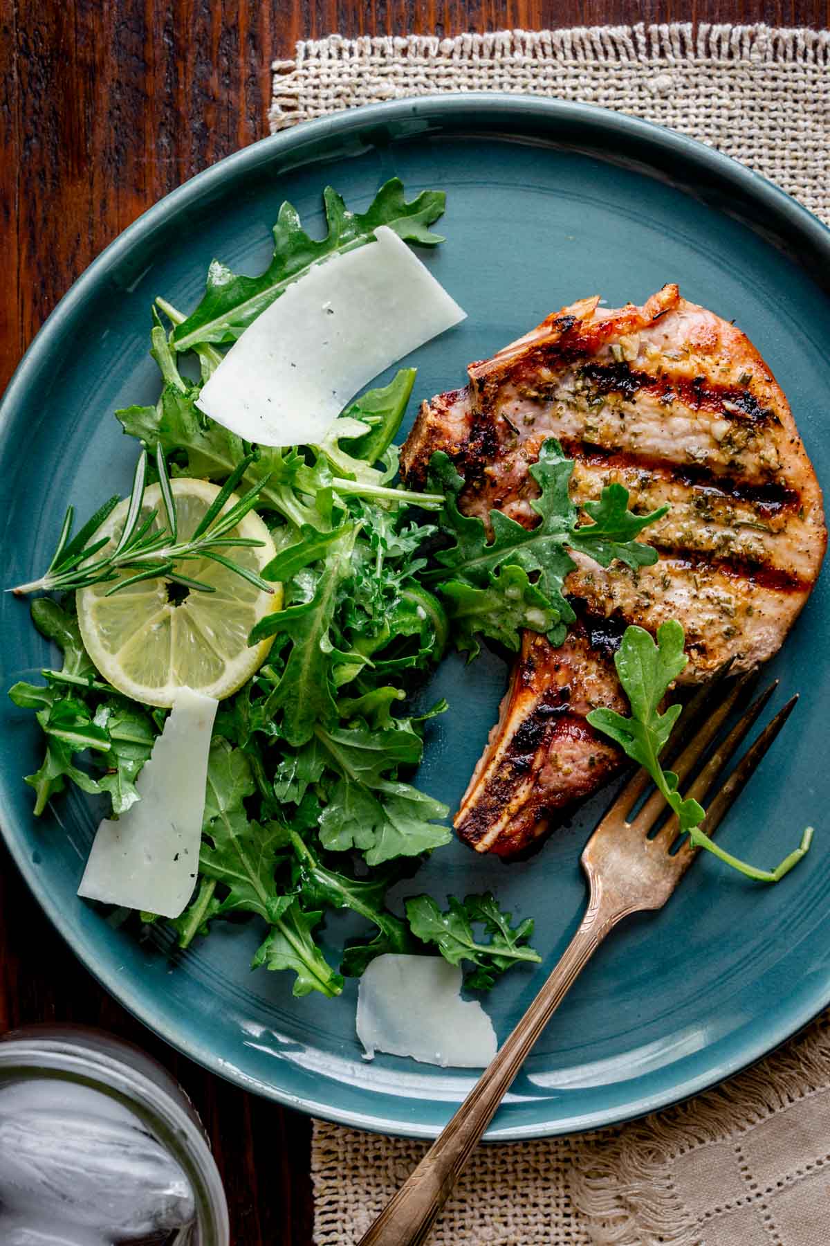 lemon rosemary pork chop on a teal plate with arugula lemon and pecorino cheese salad