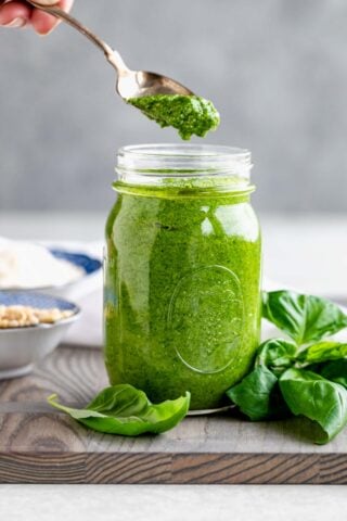 a jar with pesto, a spoon scooping out a spoonful