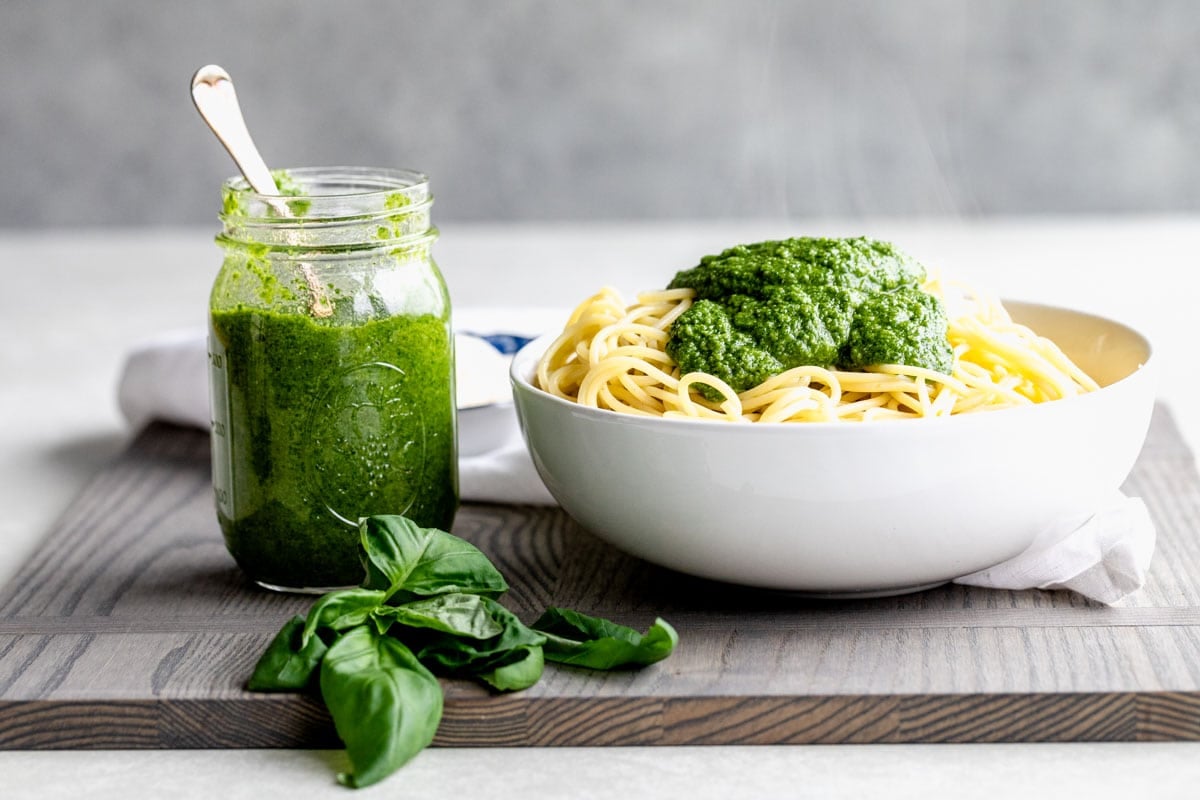 jar of pesto and pasta with pesto on top on a gray cutting board from the side