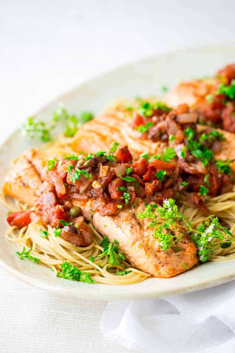 white platter with salmon on pasta with tomato sauce over it
