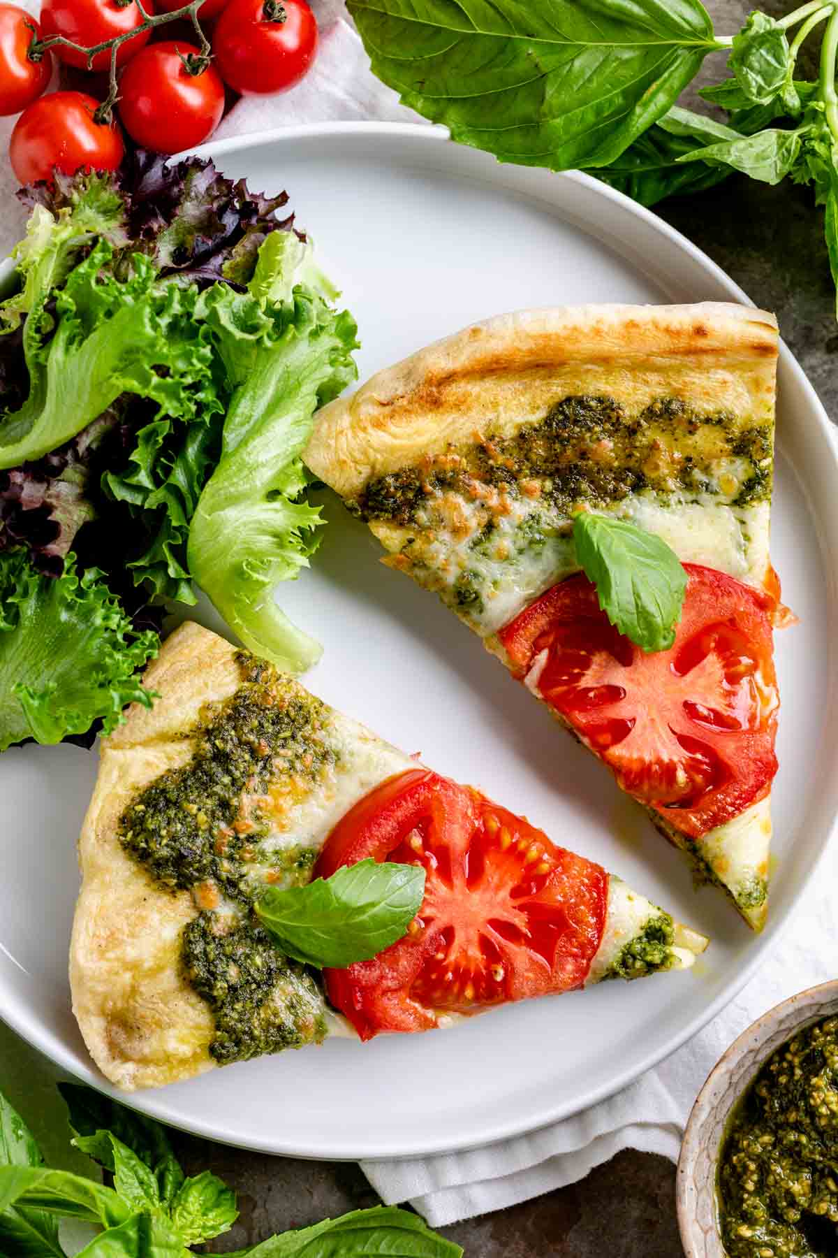 two slices of pesto pizza on a white plate with salad