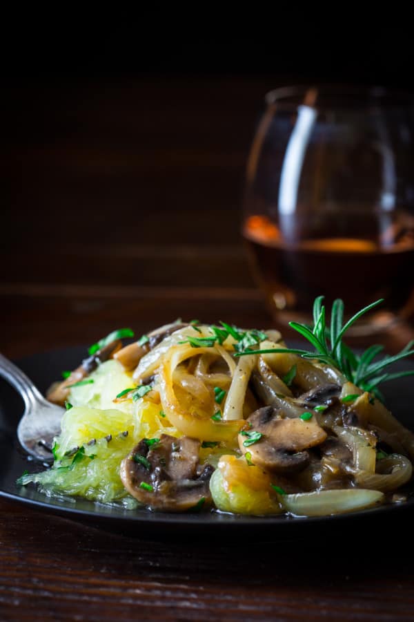 a moody table scape with a plate of spaghetti squash with onions and mushrooms on it